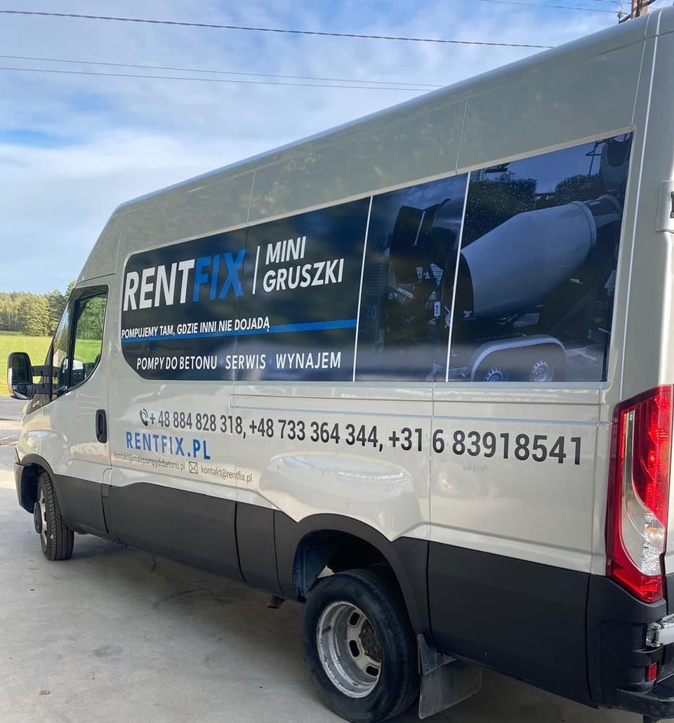 Srebrny bus z oklejeniem RENTFIX MINI GRUSZKI, widok z tyłu pod kątem: panel ze zdjęciami, trzy numery telefonów i adres rentfix.pl na burcie.