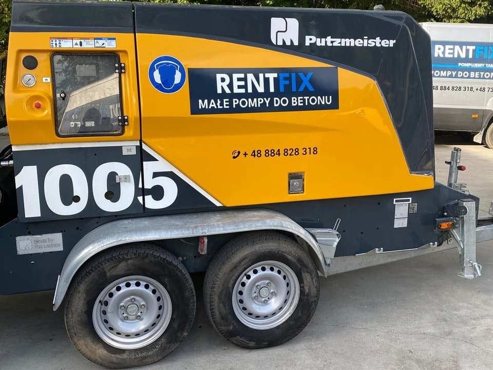 Prawy bok żółto-grafitowej pompy do betonu 1005 z naklejką RENTFIX Małe Pompy do Betonu na ocynkowanej przyczepie dwuosiowej.